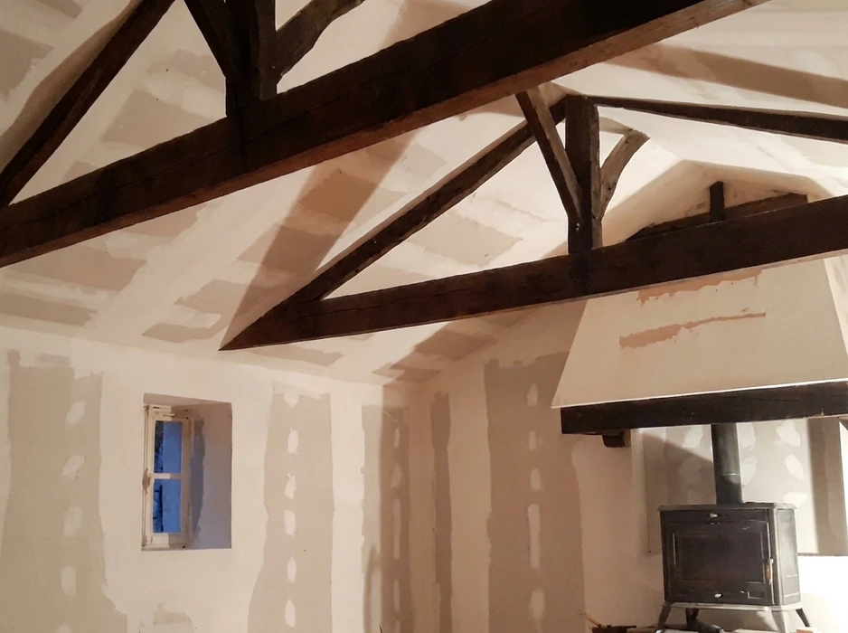 Intérieur en cours de rénovation, pièce à viande apparente avec charpente traditionnelle en bois sombre