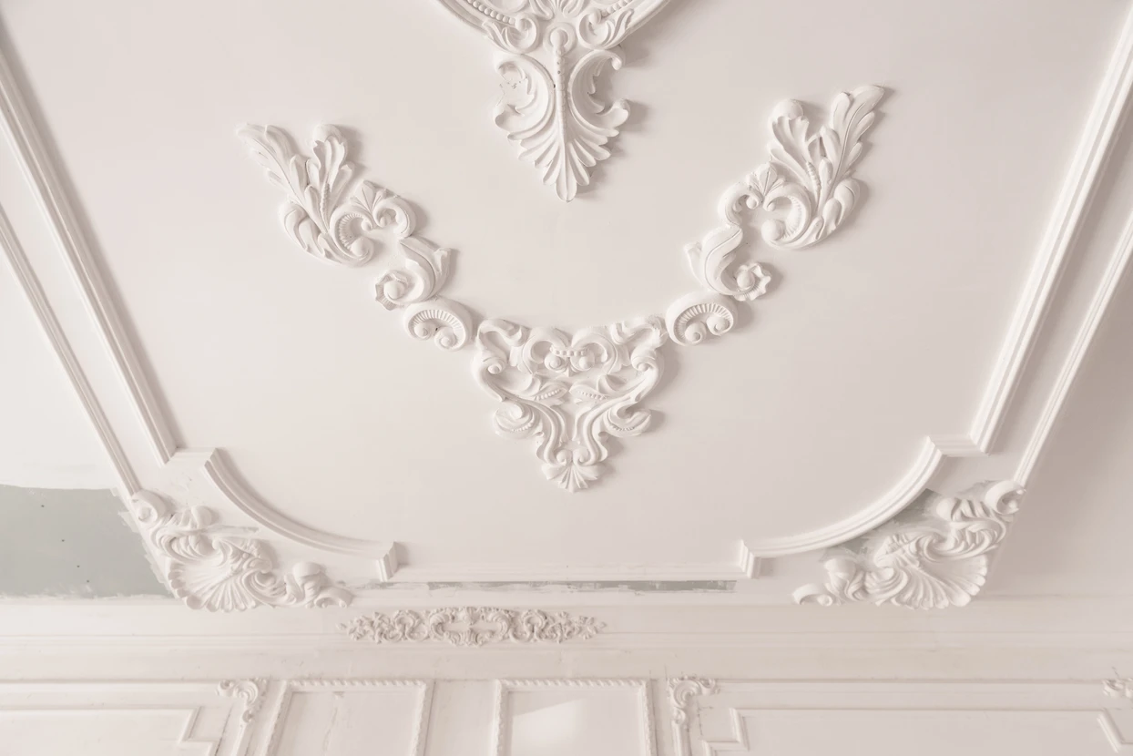 Plafond intérieur avec moulures décoratives en plâtre blanc ornées de motifs floraux et volutes baroques