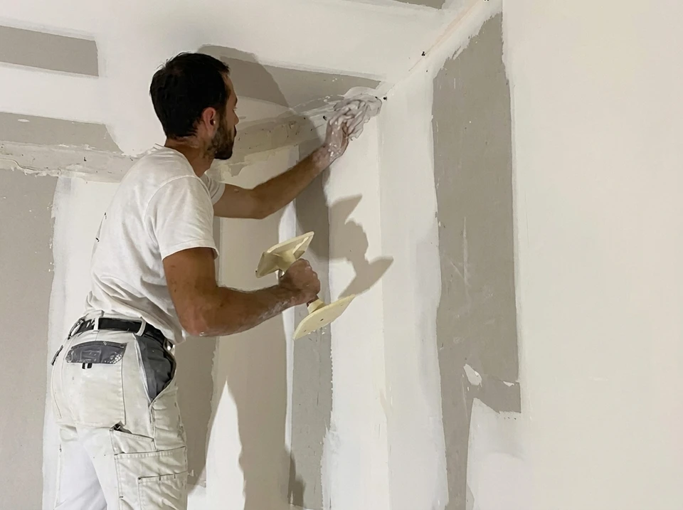 Artisan plâtrier applique de l'enduit de lissage sur un angle mur-plafond