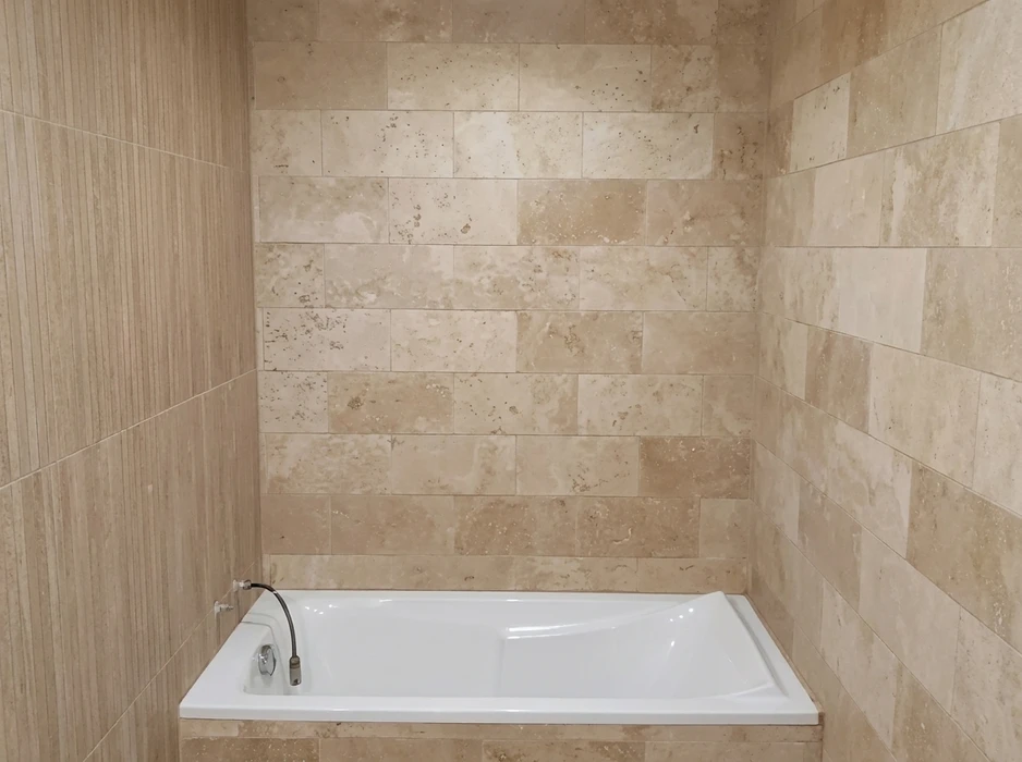 Salle de bain avec baignoire encastrée blanche, entourée de murs revêtus de carreaux en travertin beige