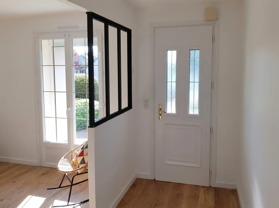 Couloir d'entrée avec deux portes : une porte à battant laquée anthracite avec poignée en acier inoxydable et serrure à cylindre, et une porte coulissante double vantail gris clair sur rail encastré en tête