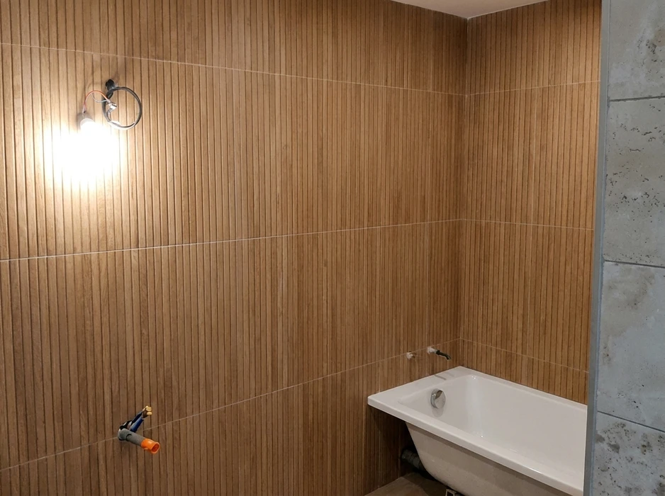 Salle de bain avec baignoire encastrée rectangulaire blanche, posée sur un podium habillé de carrelage travertin beige