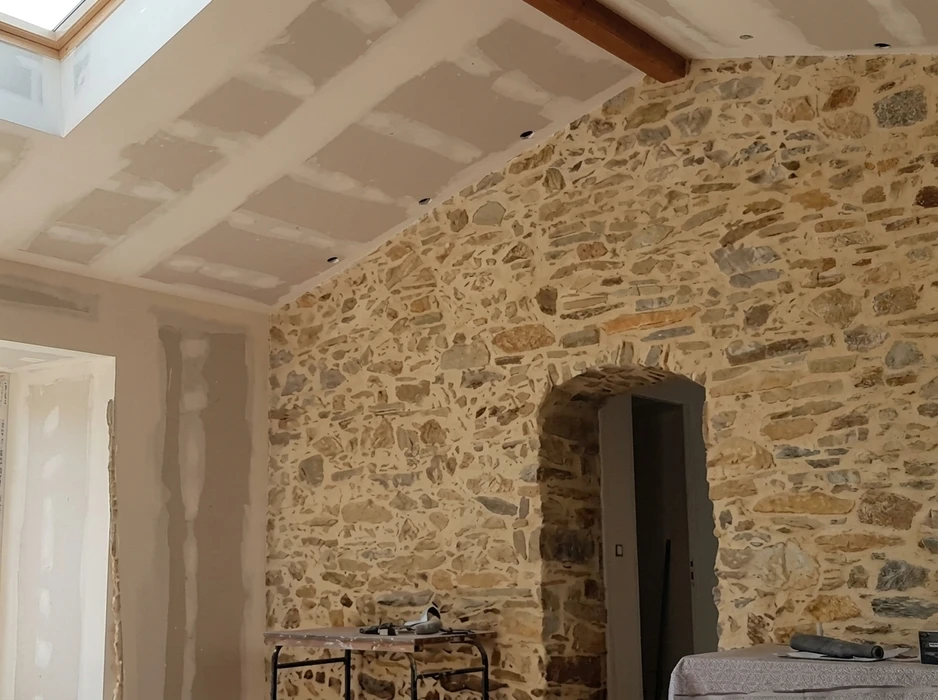 Artisan sur échasses de plaquiste travaillant l'enduit sur des cloisons en placo